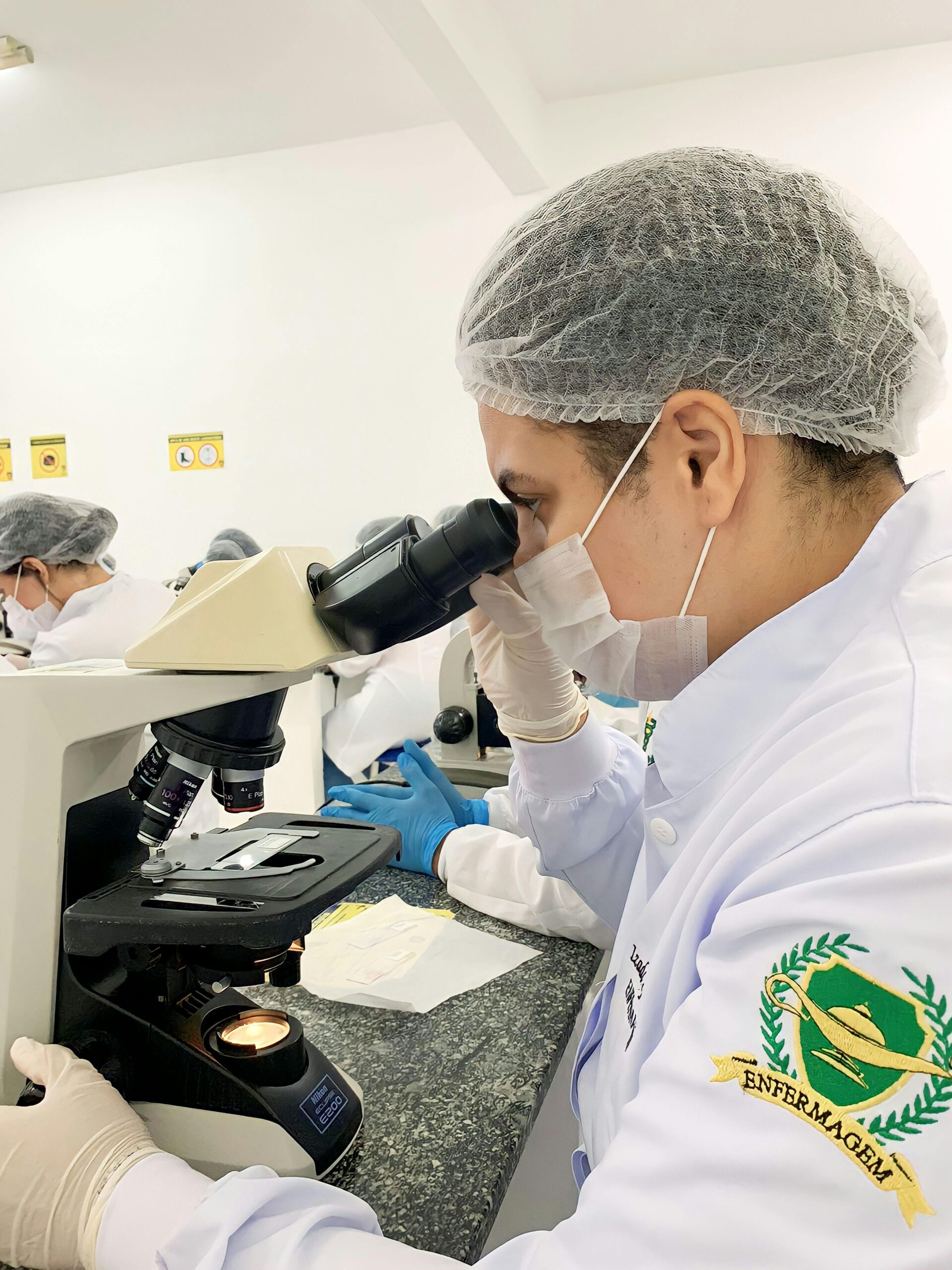 A focused lab technician examines samples under a microscope in a clinical laboratory environment.